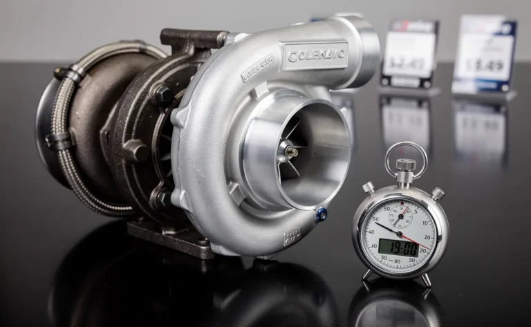 Un turbocompresseur posé sur une surface réfléchissante, accompagné d’une étiquette de prix en arrière-plan et d’un chronomètre à côté.