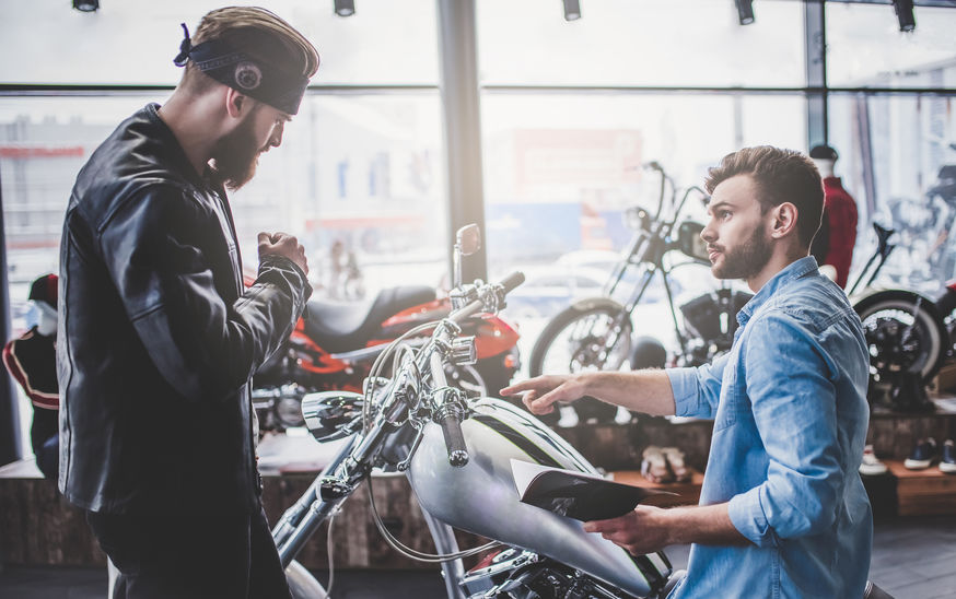 Two men in motorcycle shop. Customer and salesman. Shop assistant is helping bearded man in choosing new vehicle, motorcycle accessories and other biker stuff.