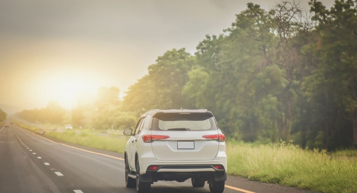 SUV blanc sur une route bordée d'arbres au soleil couchant